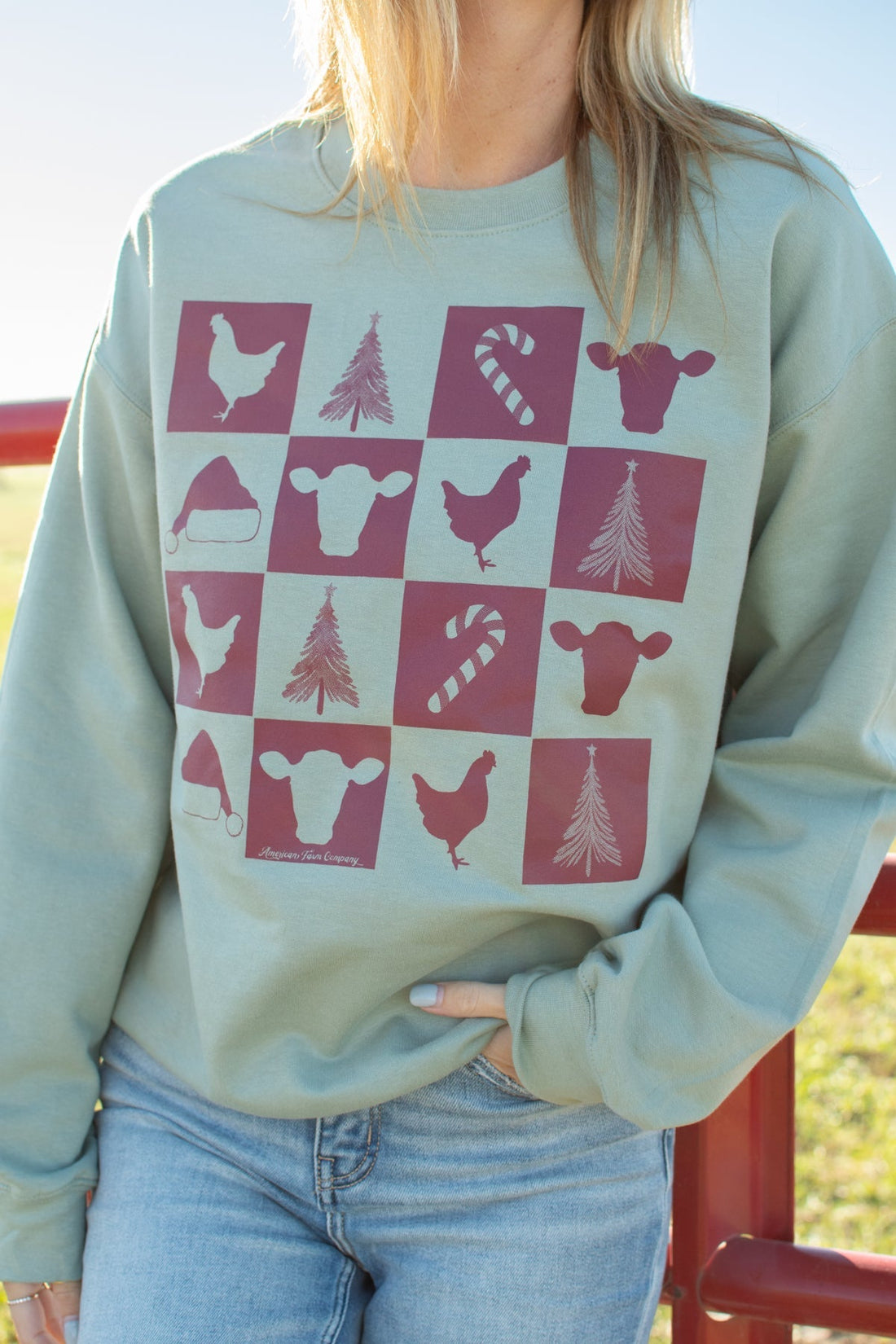 Sage green crewneck sweatshirt with relaxed fit, featuring farm animal, Christmas tree, and candy cane checkerboard graphic, embodying American Farm Company's rural heritage and agricultural lifestyle.
