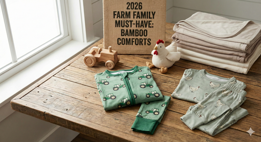 Sage green bamboo farmstead pajamas with tractor and chicken prints, heritage rural kids apparel from American Farm Company, displayed on rustic wood table beside plush hen, wooden tractor toy, and neutral bamboo blankets.