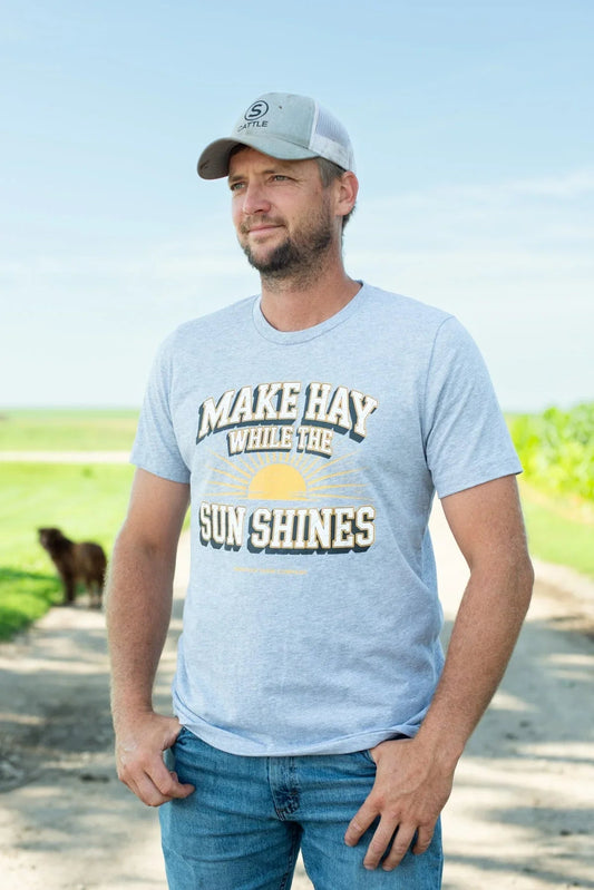 Heather grey relaxed fit tee with bold 'Make Hay While the Sun Shines' sunrise graphic, styled as rugged agricultural apparel by American Farm Company.