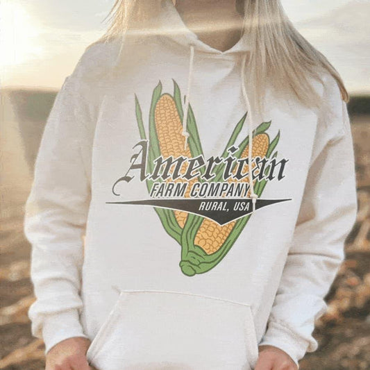 Cream heavyweight hoodie with vintage corn graphic, bold 'American Farm Company' logo, celebrates rural heritage and agricultural lifestyle.