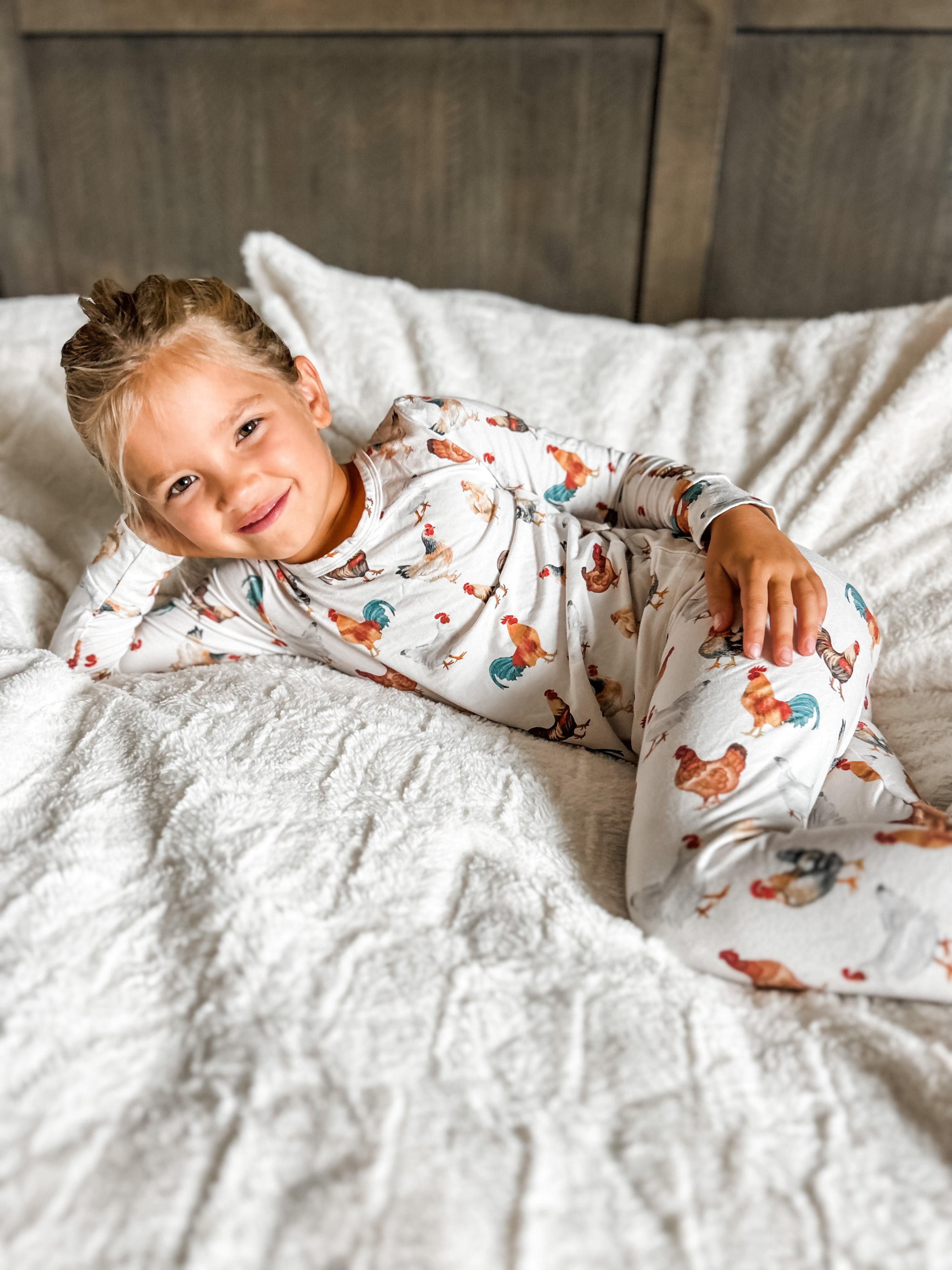 A child posing in bed wearing a set of toddler chicken pajamas
