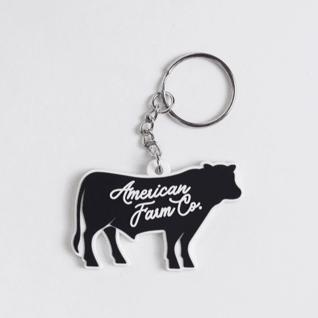 Black cow silhouette keychain with white 'American Farm Co.' script, evoking rural heritage charm.