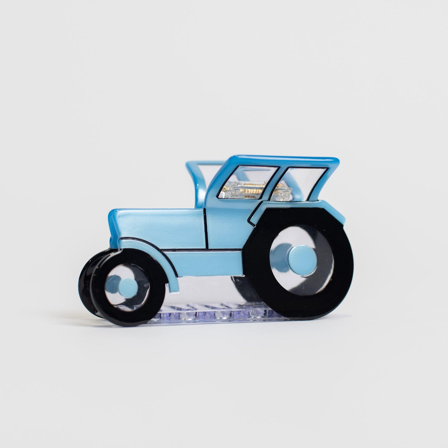Glossy blue tractor-shaped acrylic hair clip with bold black wheels, channeling rural heritage style from American Farm Company.