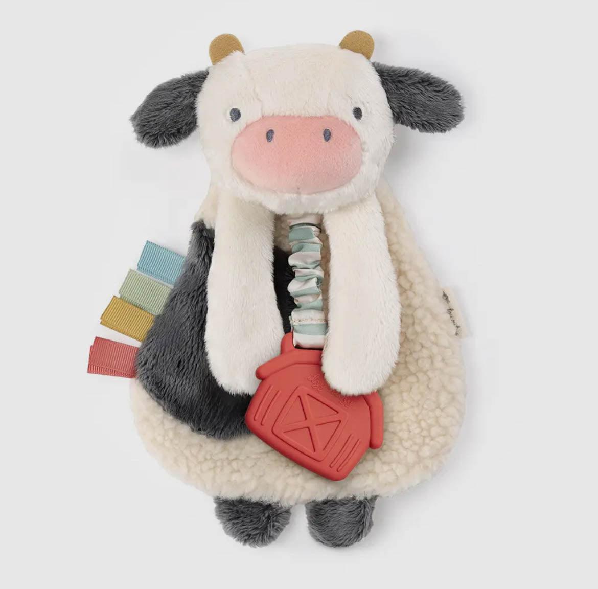 Plush black and white cow toy with sherpa fleece texture, pastel ribbon details, and red farmhouse teether, embodying rural heritage charm for American Farm Company.
