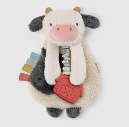 Plush black and white cow toy with sherpa fleece texture, pastel ribbon details, and red farmhouse teether, embodying rural heritage charm for American Farm Company.