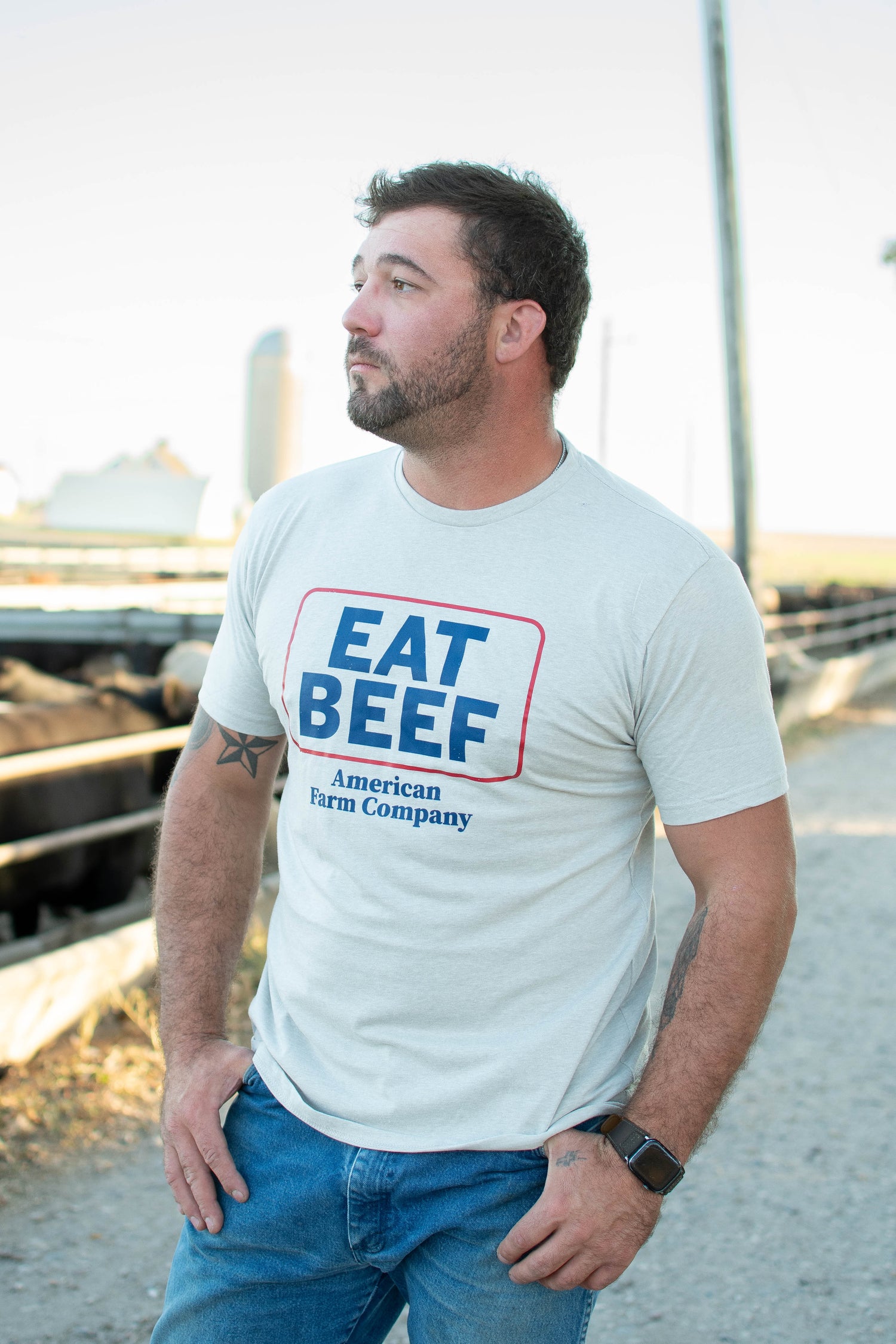 Heritage-inspired grey cotton rural tee with bold blue 'EAT BEEF' graphic, farmstead backdrop
