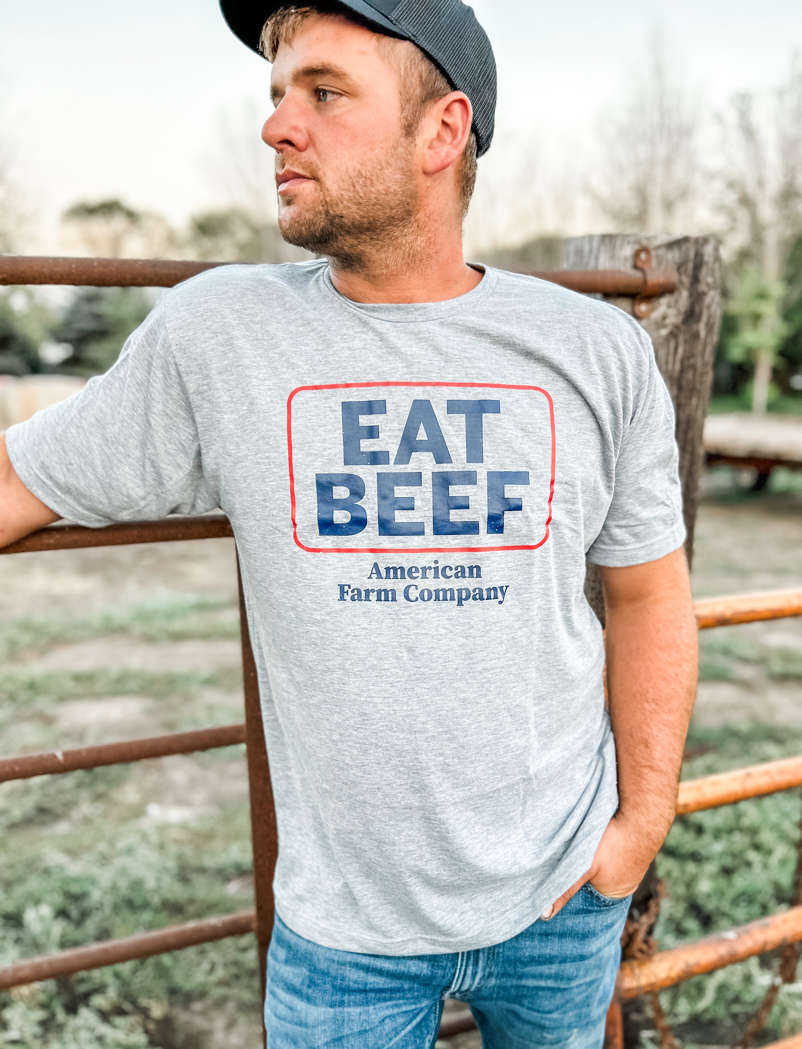 A man in the field wearing jeans, a cap, and an Eat Beef Shirt