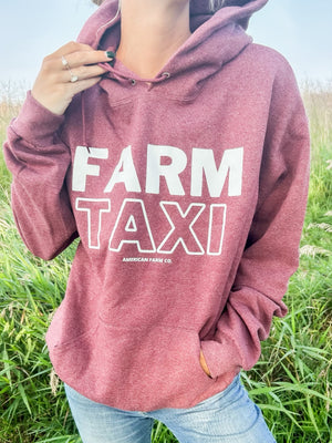 A woman in the field wearing a Farm Taxi Hoodie paired with light jeans captured from the front view