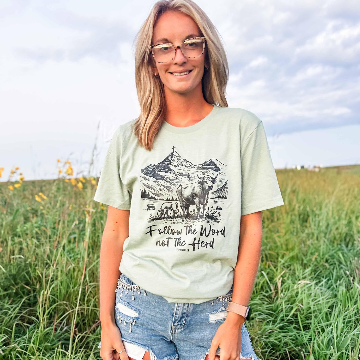 Heritage sage tee with relaxed fit, featuring mountain cow graphic and 'Follow the Word not the Herd' script, embodying rural American Farm Company legacy.