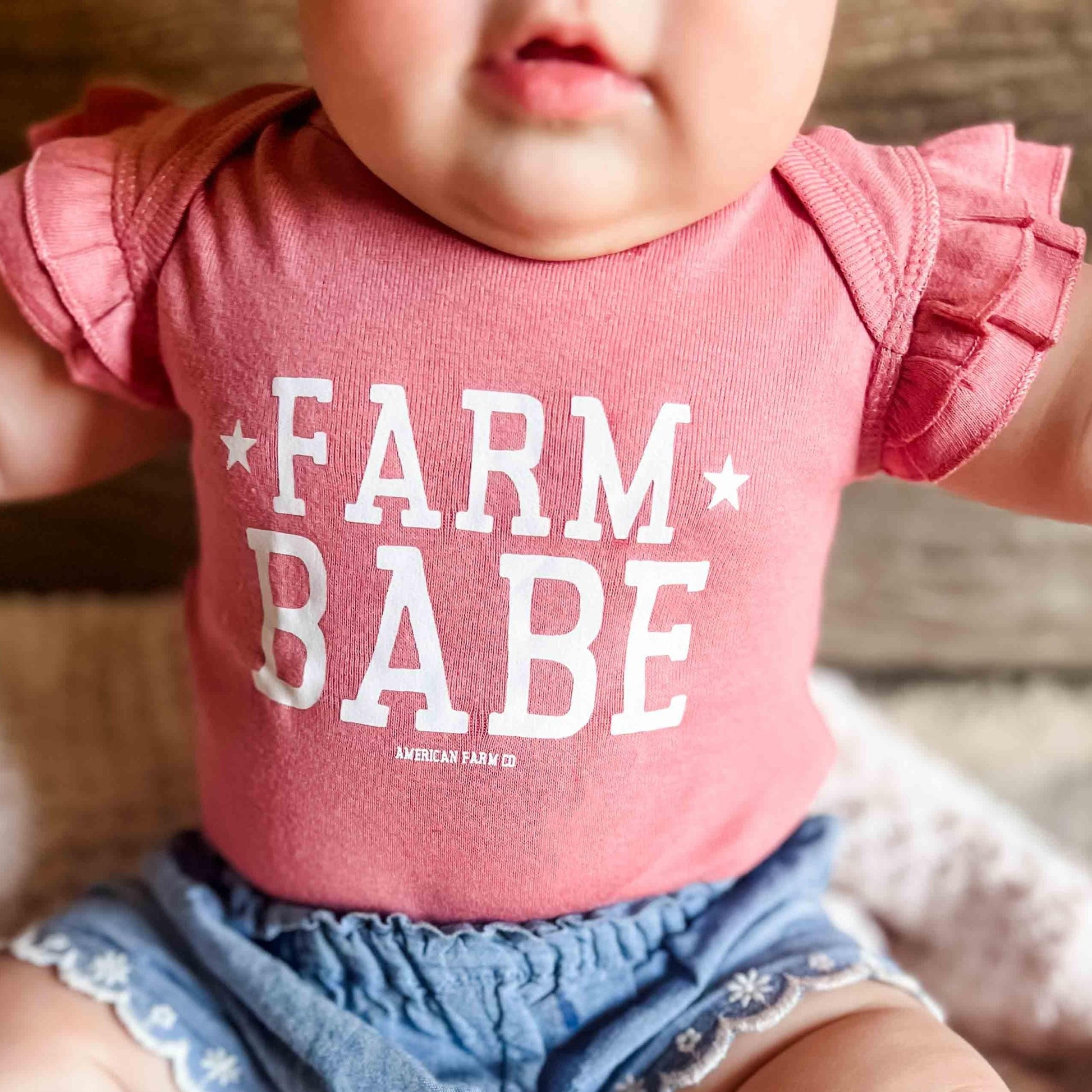 Heritage-inspired mauve ruffle sleeve baby onesie with bold 'Farm Babe' graphic, rural legacy apparel
