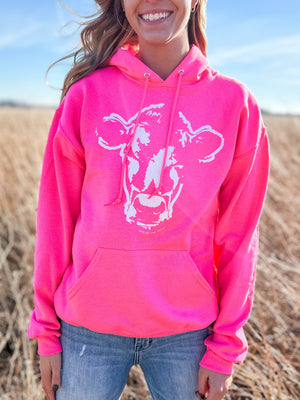 Woman in the field rocking a Neon Pink Watercolor Cow Print Hoodie and jeans for a trendy look