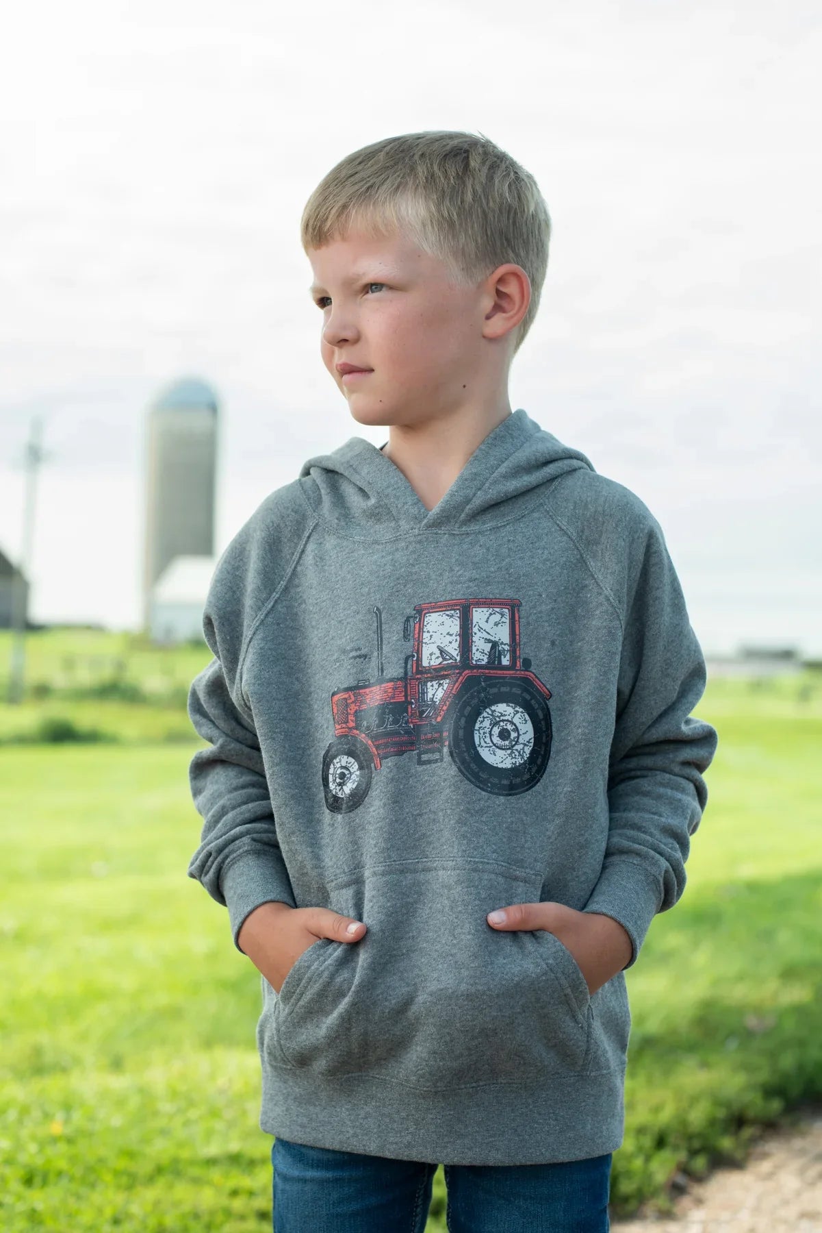 Youth wearing relaxed fit grey hoodie with vintage red tractor graphic, celebrating rural legacy by American Farm Company