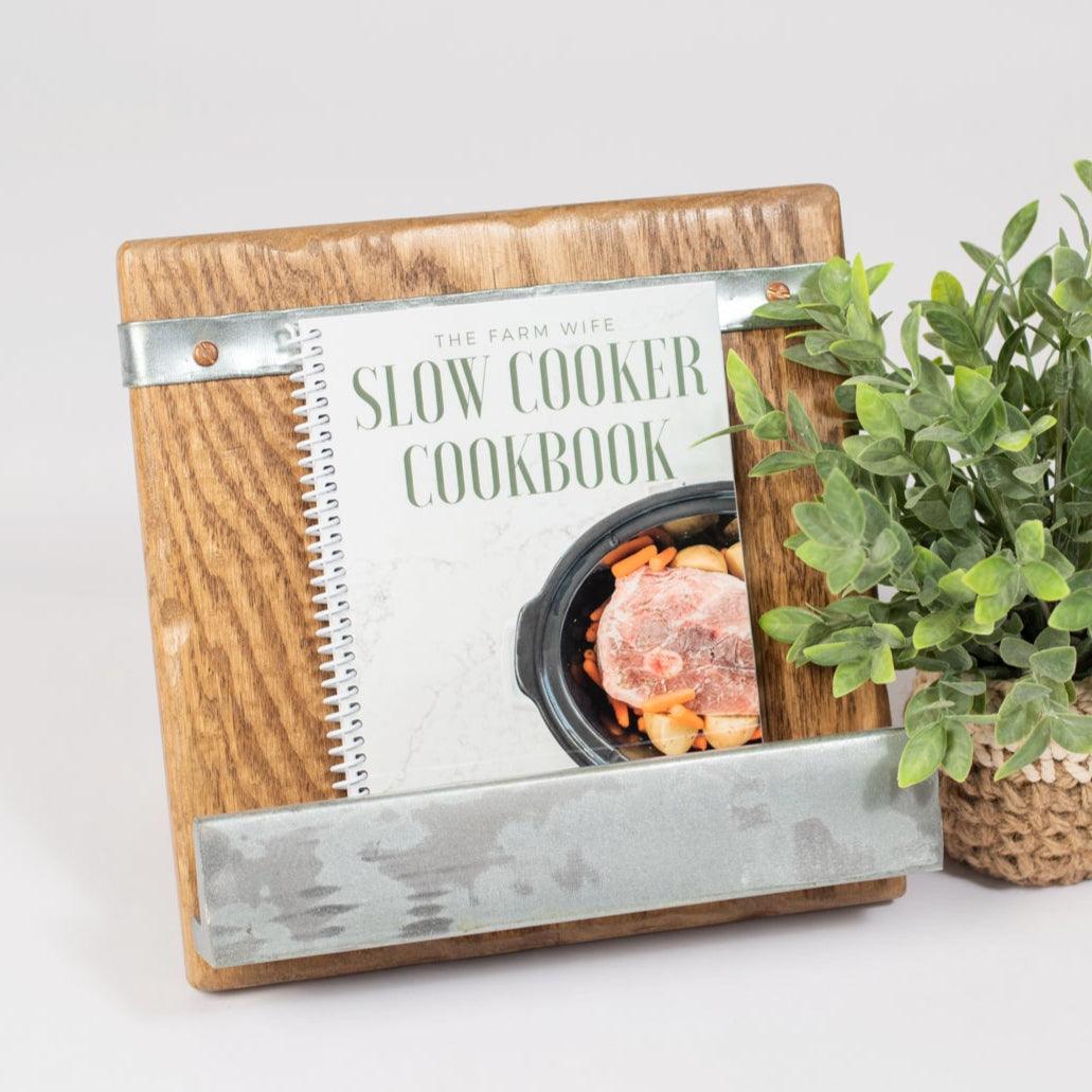 Rustic wood cookbook stand with galvanized accents, holding a slow cooker recipe book, styled beside a woven plant for a modern farmhouse kitchen vibe.