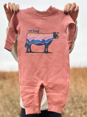 A close up view of a woman flaunting a Retro Cow Baby Fleece Onesie in the field