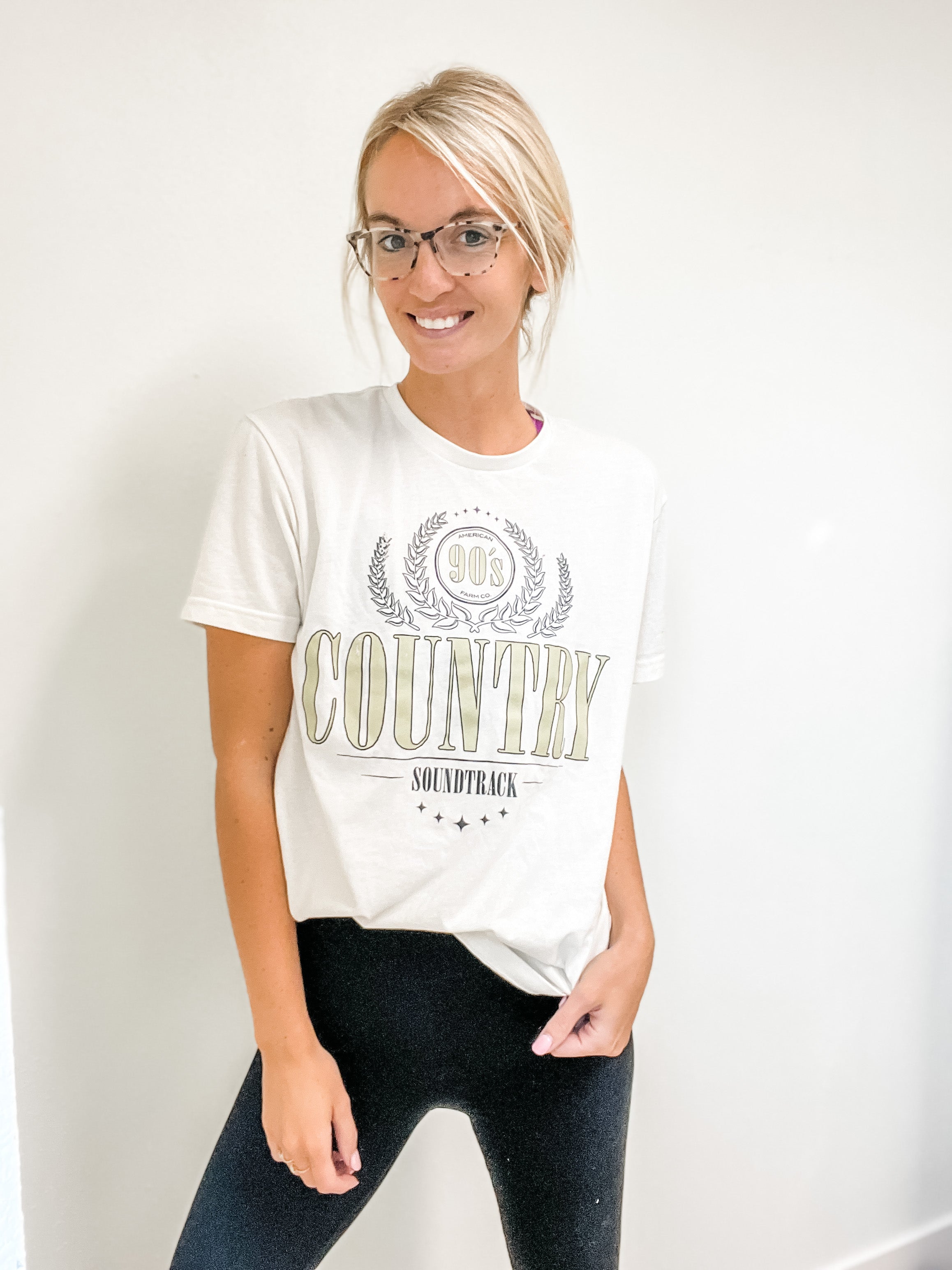 A woman in leggings wearing 90s Country T-shirts with white backdrop