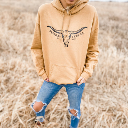 A woman wearing a Skull Horn Hoodie and ripped jeans in the field seen from the front