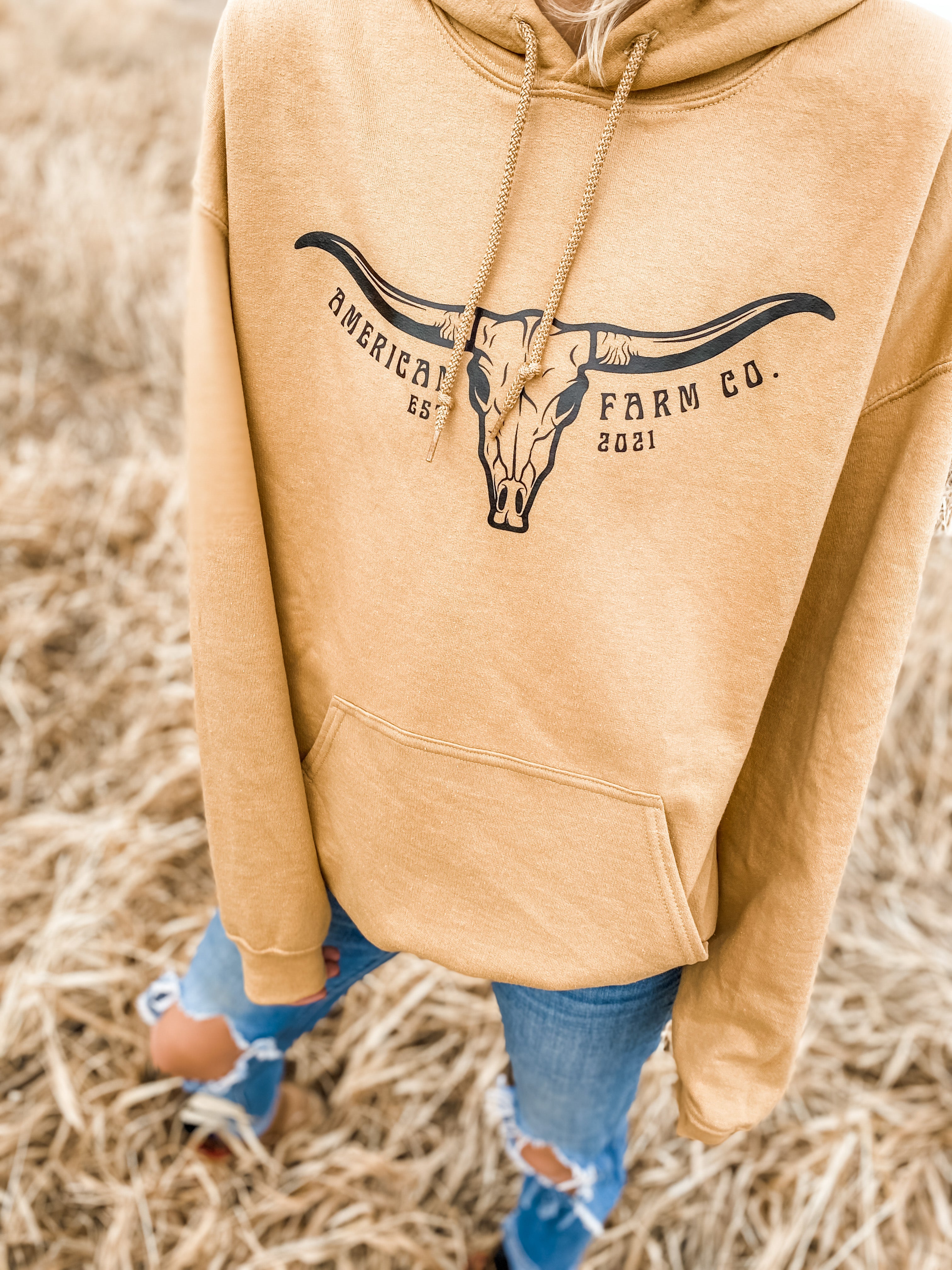 Front view of Skull Horn Hoodie worn by a woman paired with ripped jeans in the field