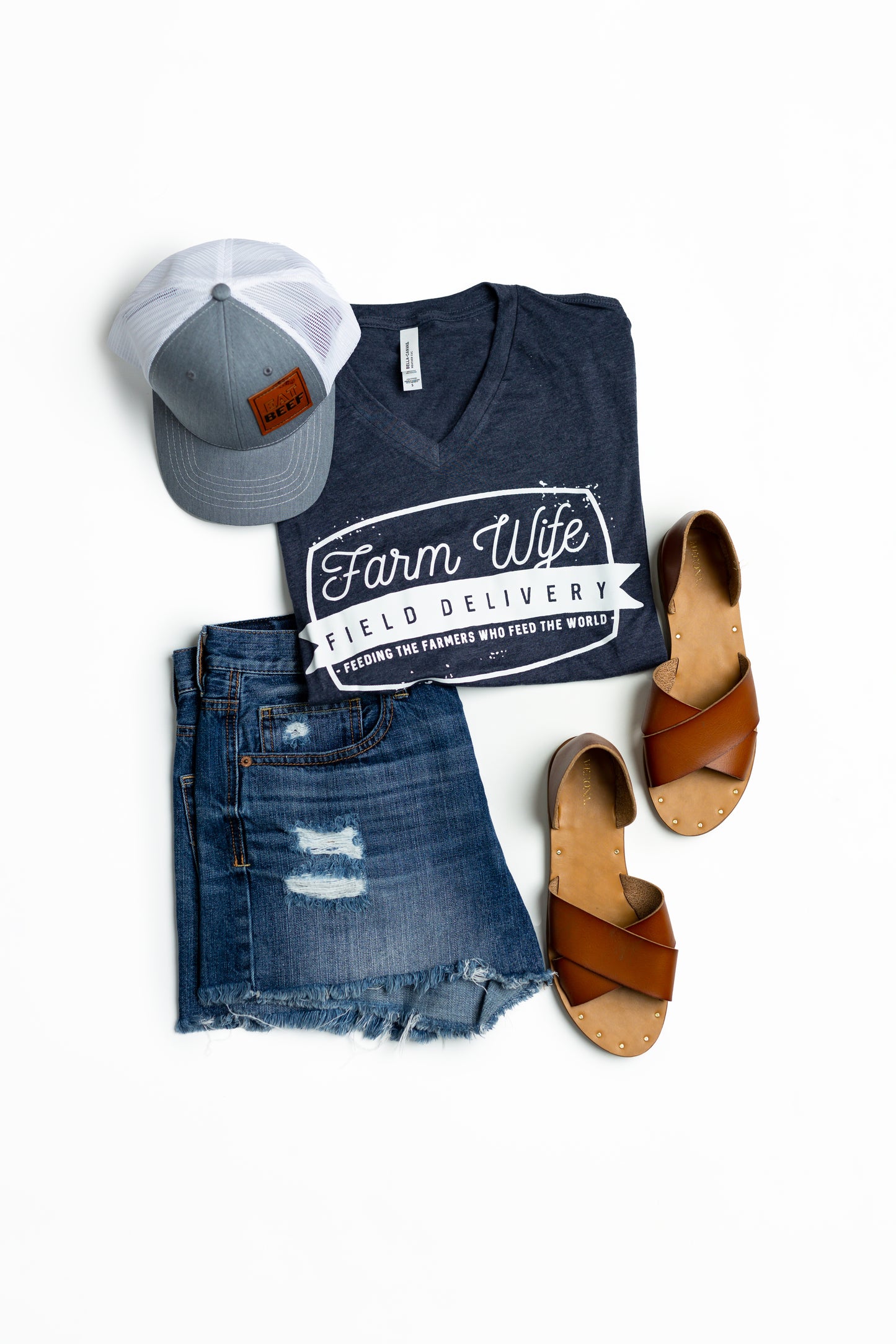 A complete outfit featuring Farm Wife V Neck, a denim short, a grey cap, and brown sandals, creating a casual yet trendy look for a day out
