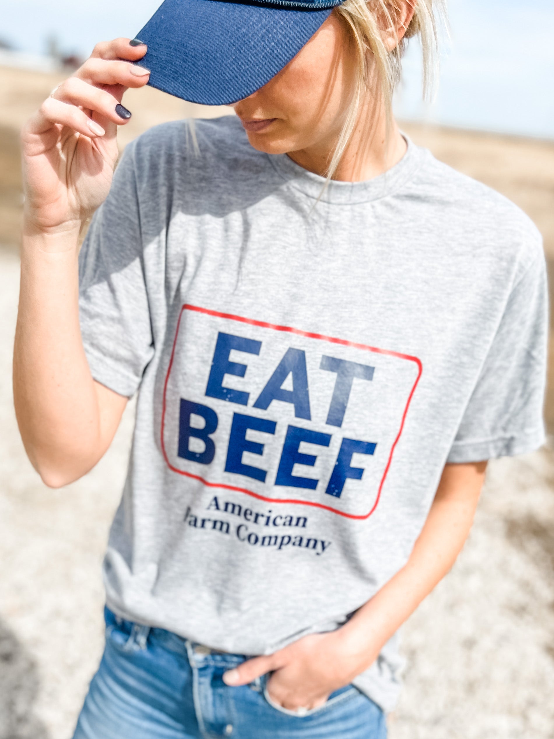 A woman in jeans and a cap donning an Eat Beef Shirt in the field