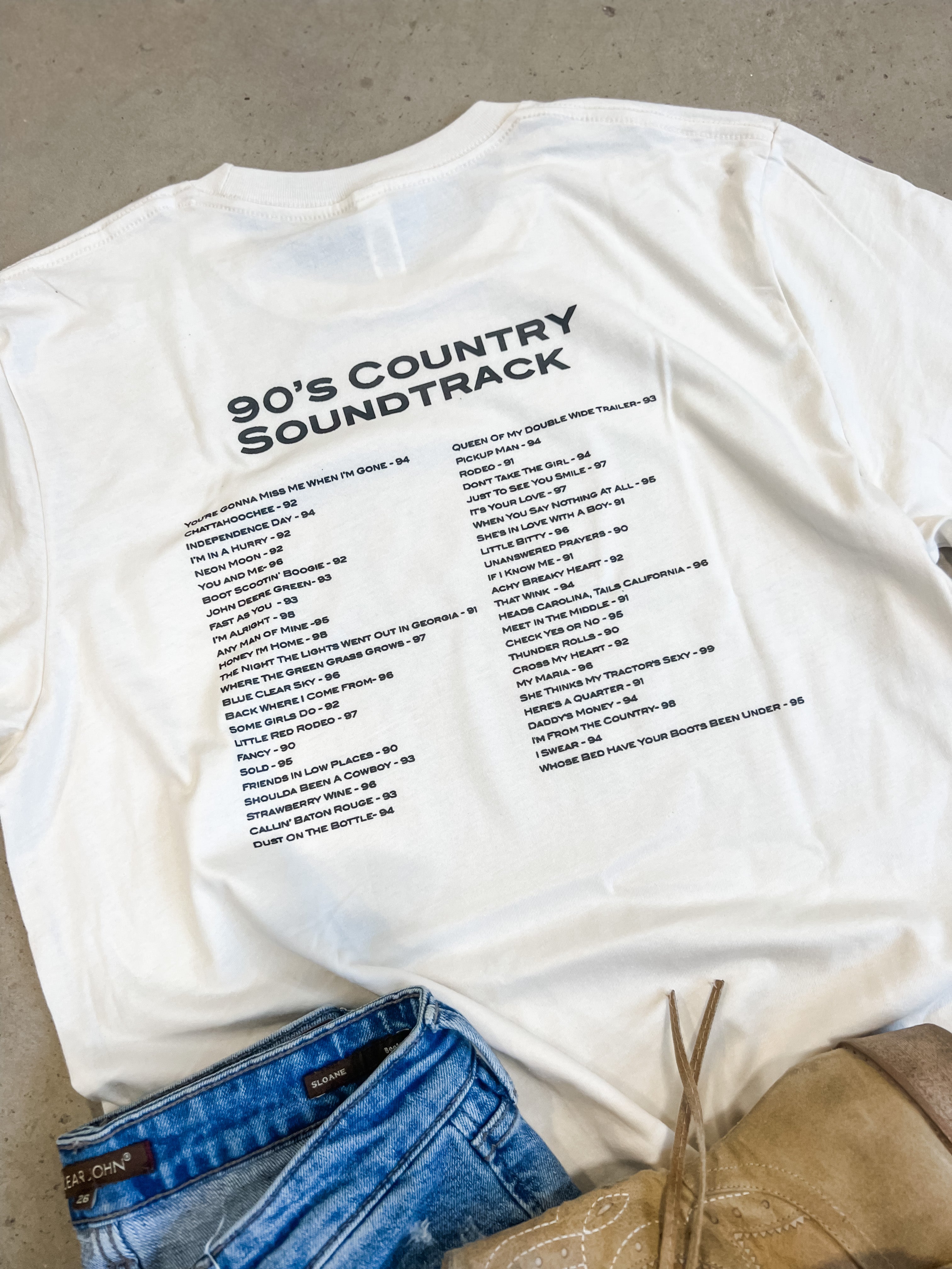 Back of 90s Country T-Shirts flat lay with jeans and boots beside